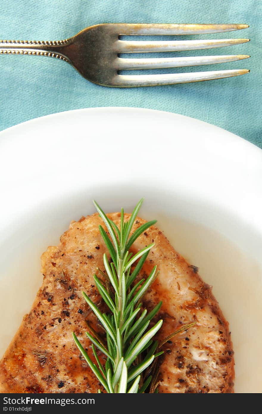 Rosemary chicken breast on a white plate with blue cloth background. Rosemary chicken breast on a white plate with blue cloth background.