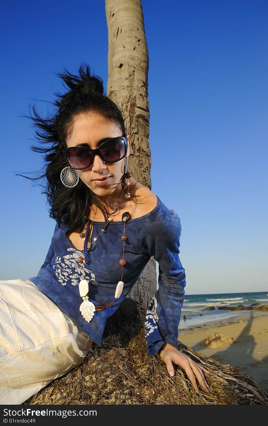 Portrait of young woman on the beach leaning against palm tree trunk. Portrait of young woman on the beach leaning against palm tree trunk