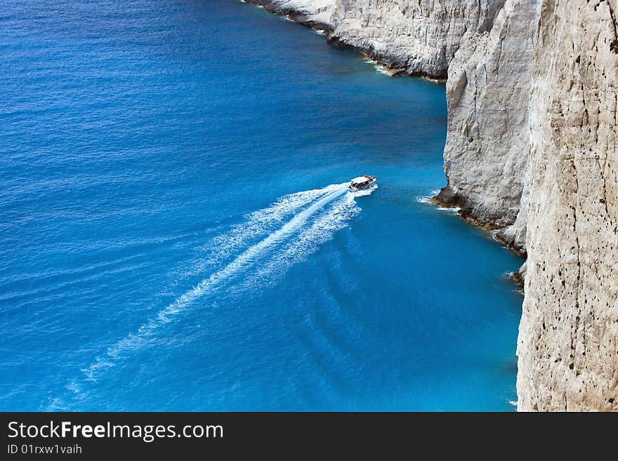 Motor boat infront of a rocky coastline seamed with amazing blue colored water.