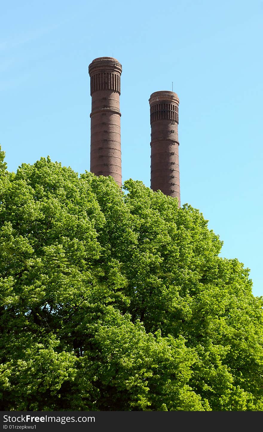 Old factory pipes and green trees against the blue sky. Old factory pipes and green trees against the blue sky.