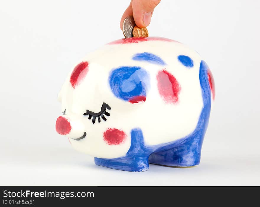 Fingers add coins to a piggy bank; isolated on a white background. Fingers add coins to a piggy bank; isolated on a white background.