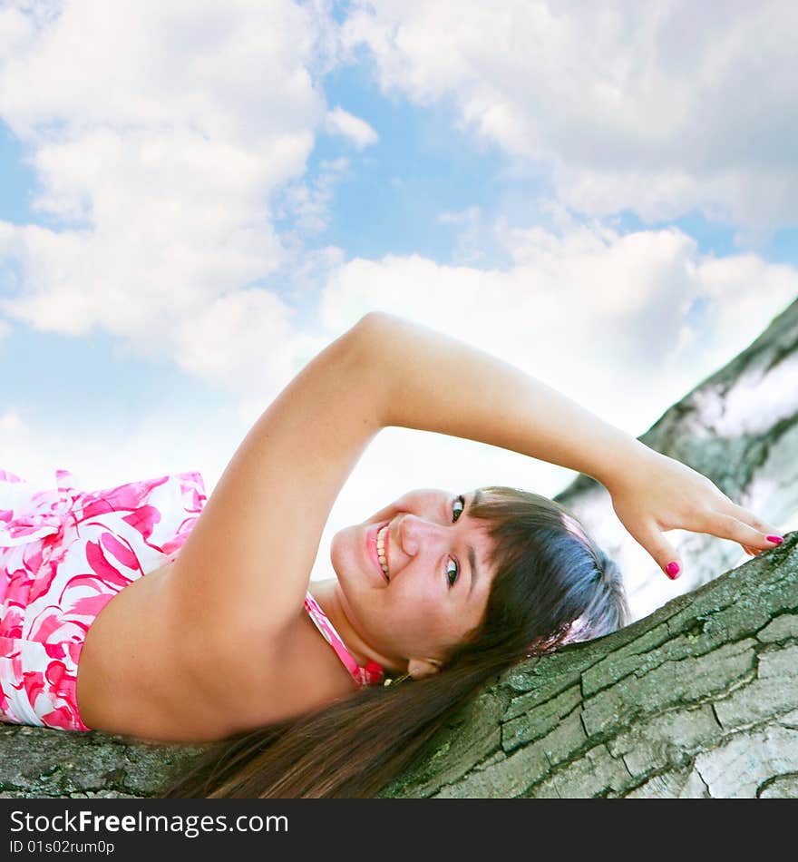 Young attractive girl laying on tree on sky background