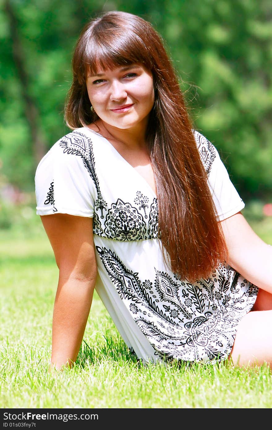 Young attractive girl sitting on green grass in park