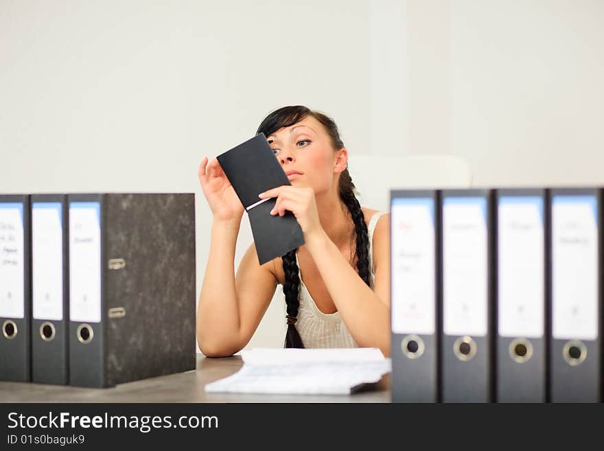 Businesswoman puting on her make up with mirror making her eye lashes and eye brows to beautify herself in office sitting on desk with a lot of work. Businesswoman puting on her make up with mirror making her eye lashes and eye brows to beautify herself in office sitting on desk with a lot of work.