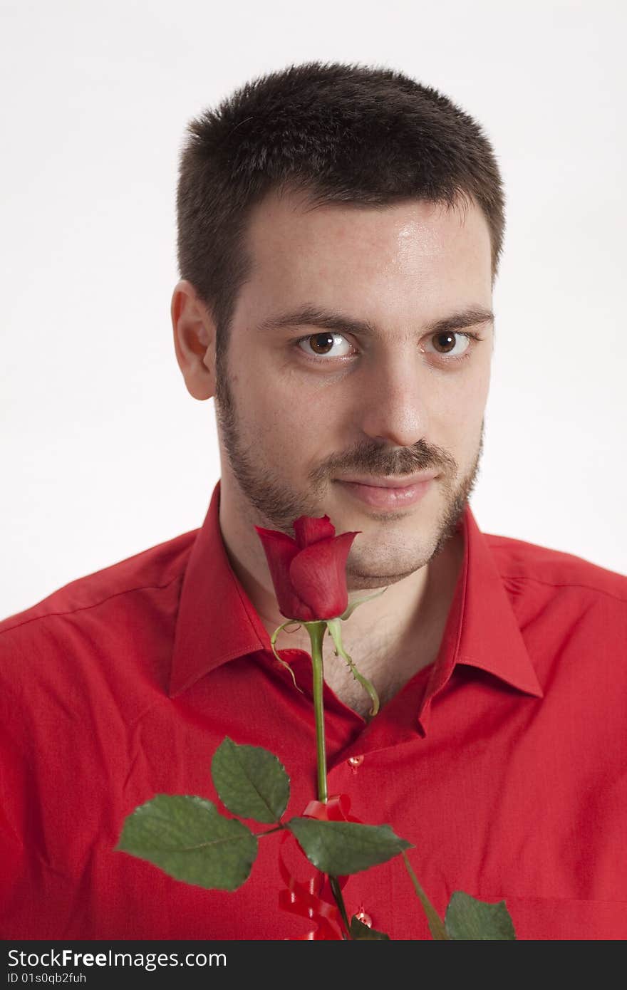 Young, handsome man in red shirt, holding a beautiful red rose in front of his mouth. Young, handsome man in red shirt, holding a beautiful red rose in front of his mouth