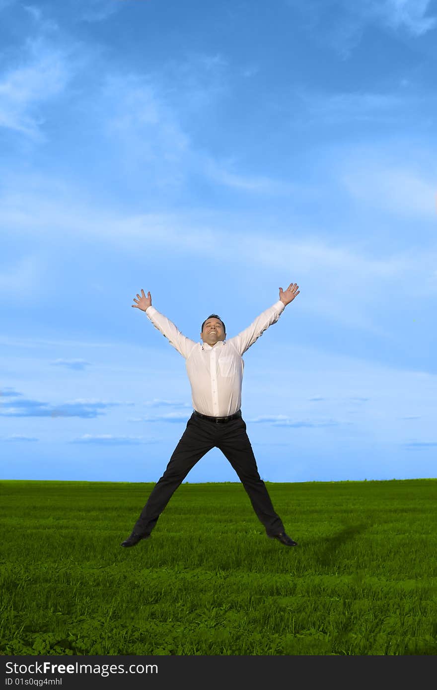 Businessman jumping on the green grass over clouds blue sky