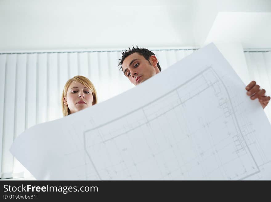 Two architects examining blueprint indoors. Low angle view. Copy space