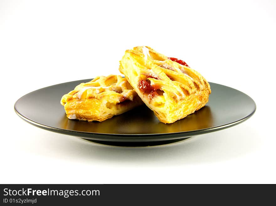 Raspberry and custard danish on a black plate on a white background. Raspberry and custard danish on a black plate on a white background