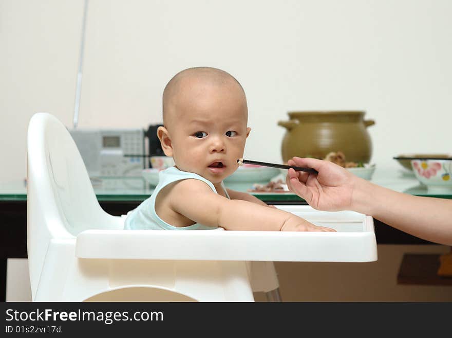 A Chinese mother is feeding baby in highchair.