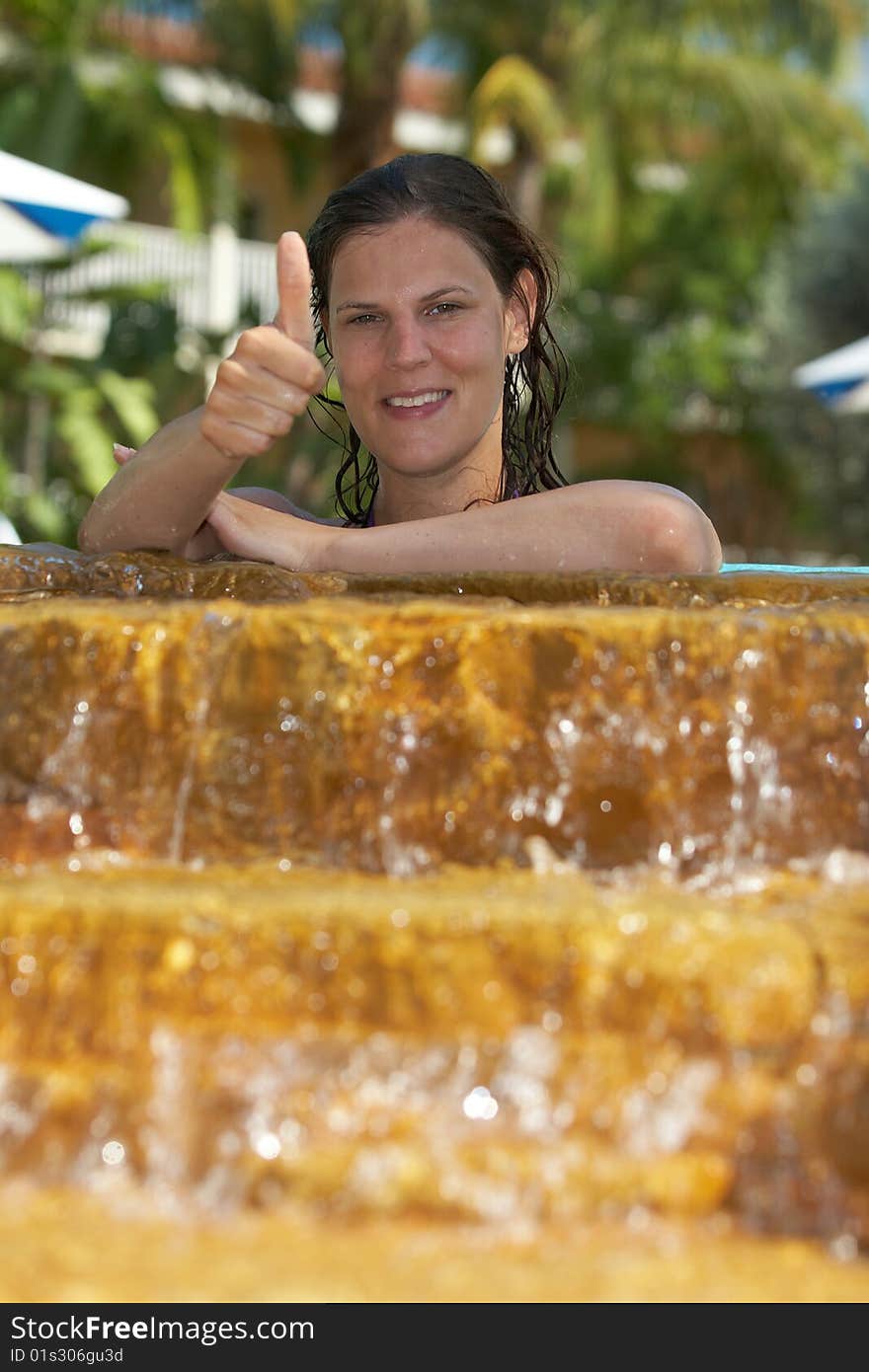 Young woman in a beautiful pool with palms in the background. She is showing a thumbs up sign. Young woman in a beautiful pool with palms in the background. She is showing a thumbs up sign.