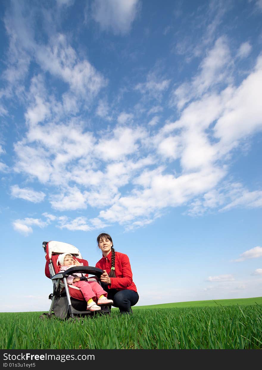 Woman with a baby-buggy in the field under blue sky with clouds. Woman with a baby-buggy in the field under blue sky with clouds