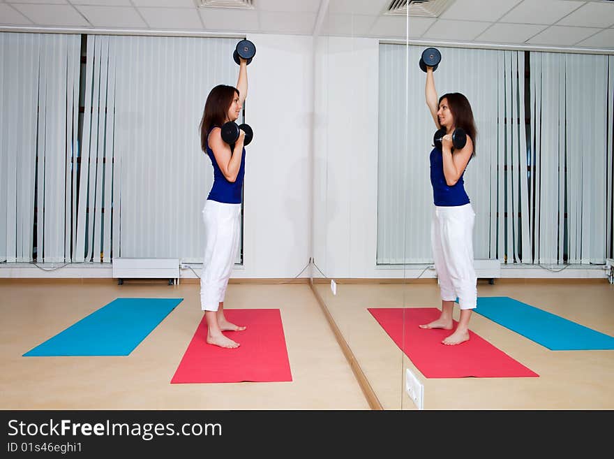 Girl carries out exercises with dumbbells in sports hall. Girl carries out exercises with dumbbells in sports hall