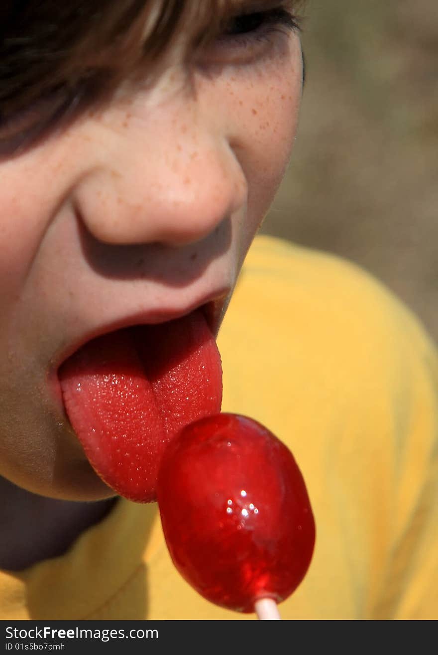 Close up of a young boy enjoying a red lollipop on a summer day