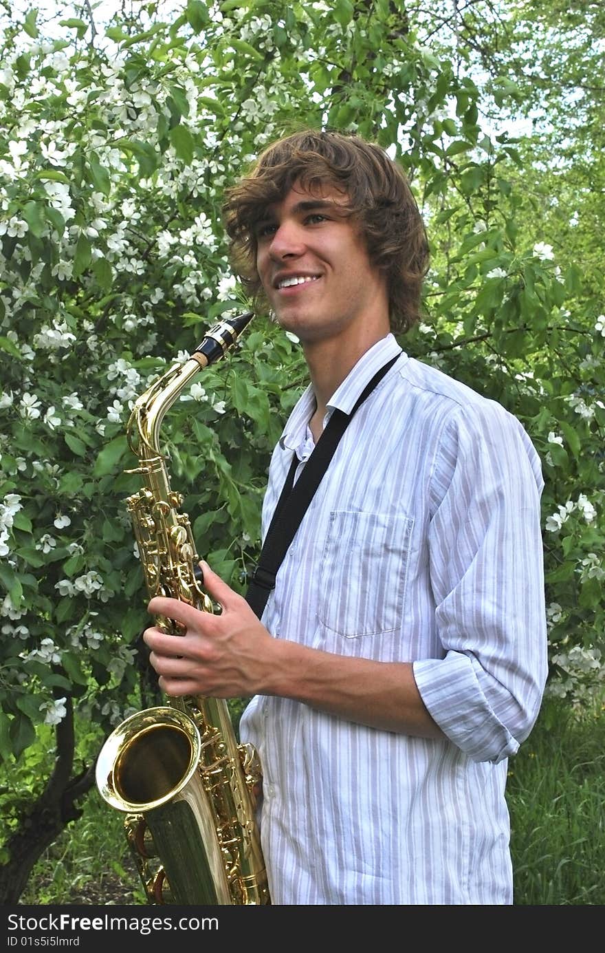 Beautiful boy with saxophone on background of flowering apple-tree. Beautiful boy with saxophone on background of flowering apple-tree