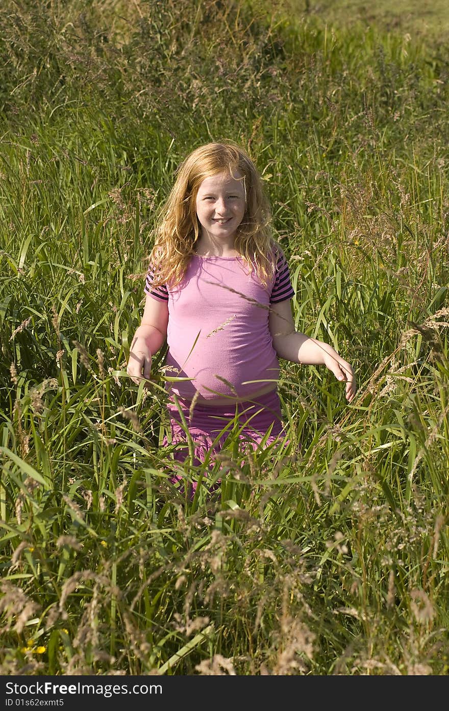 Little girl in pink clothes between high grass