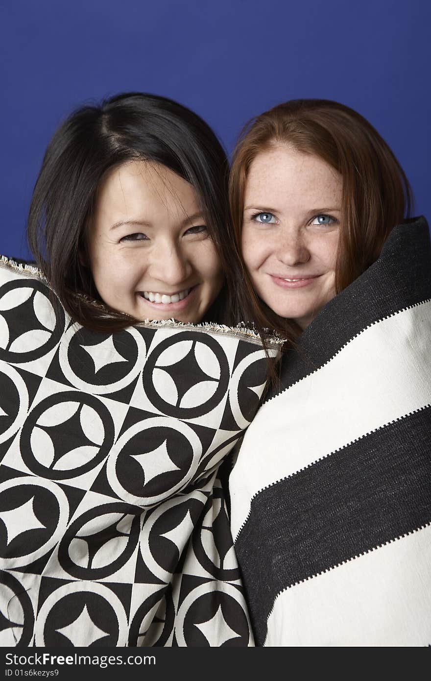 Two young women, one Asian, the other Caucasian, head to head smiling wearing black and white patterned shawls. Two young women, one Asian, the other Caucasian, head to head smiling wearing black and white patterned shawls.