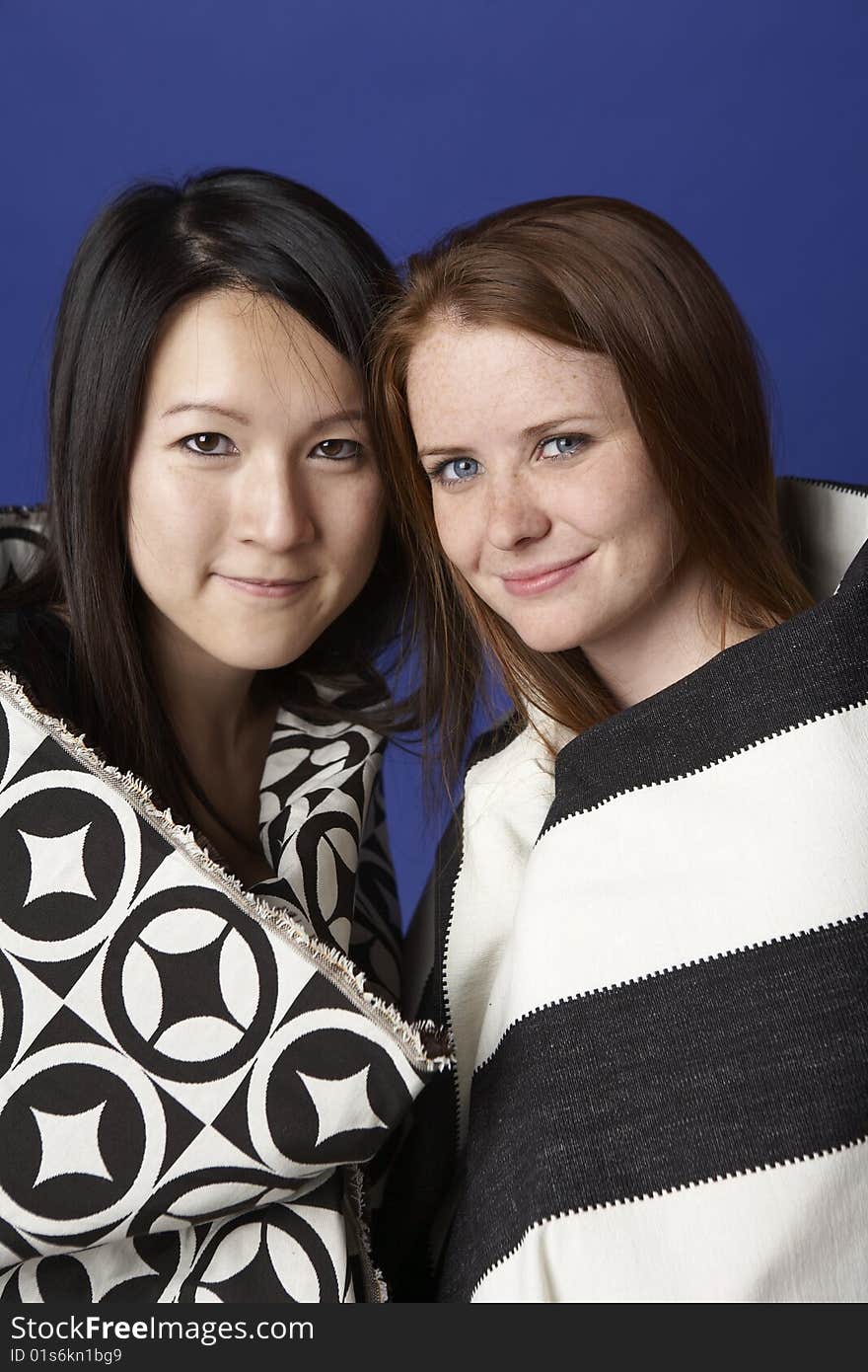 Two young women, one Asian, the other Caucasian, smile at the viewer wearing two patterned shawls. Two young women, one Asian, the other Caucasian, smile at the viewer wearing two patterned shawls.