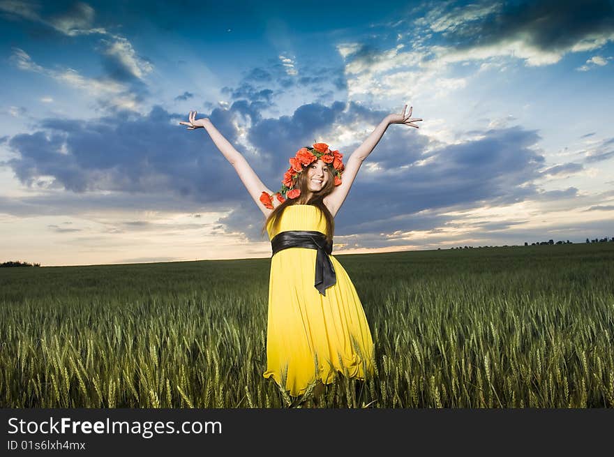 Beautiful young girl in floral wreath in the wheat field, low angle view. Beautiful young girl in floral wreath in the wheat field, low angle view