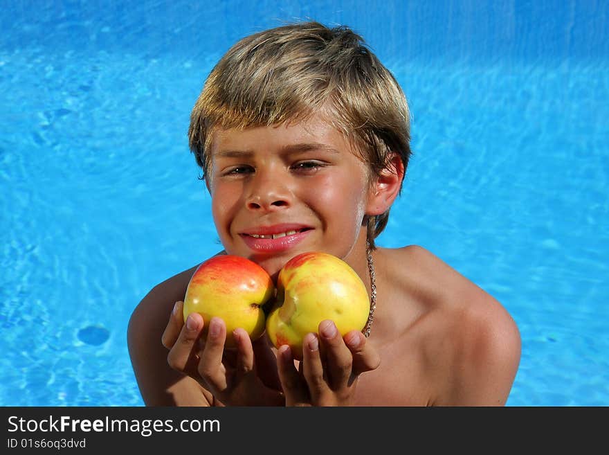 A 10 year old American - German boy sitting at a swimming pool and presenting delicious apples in the summer sun. A 10 year old American - German boy sitting at a swimming pool and presenting delicious apples in the summer sun