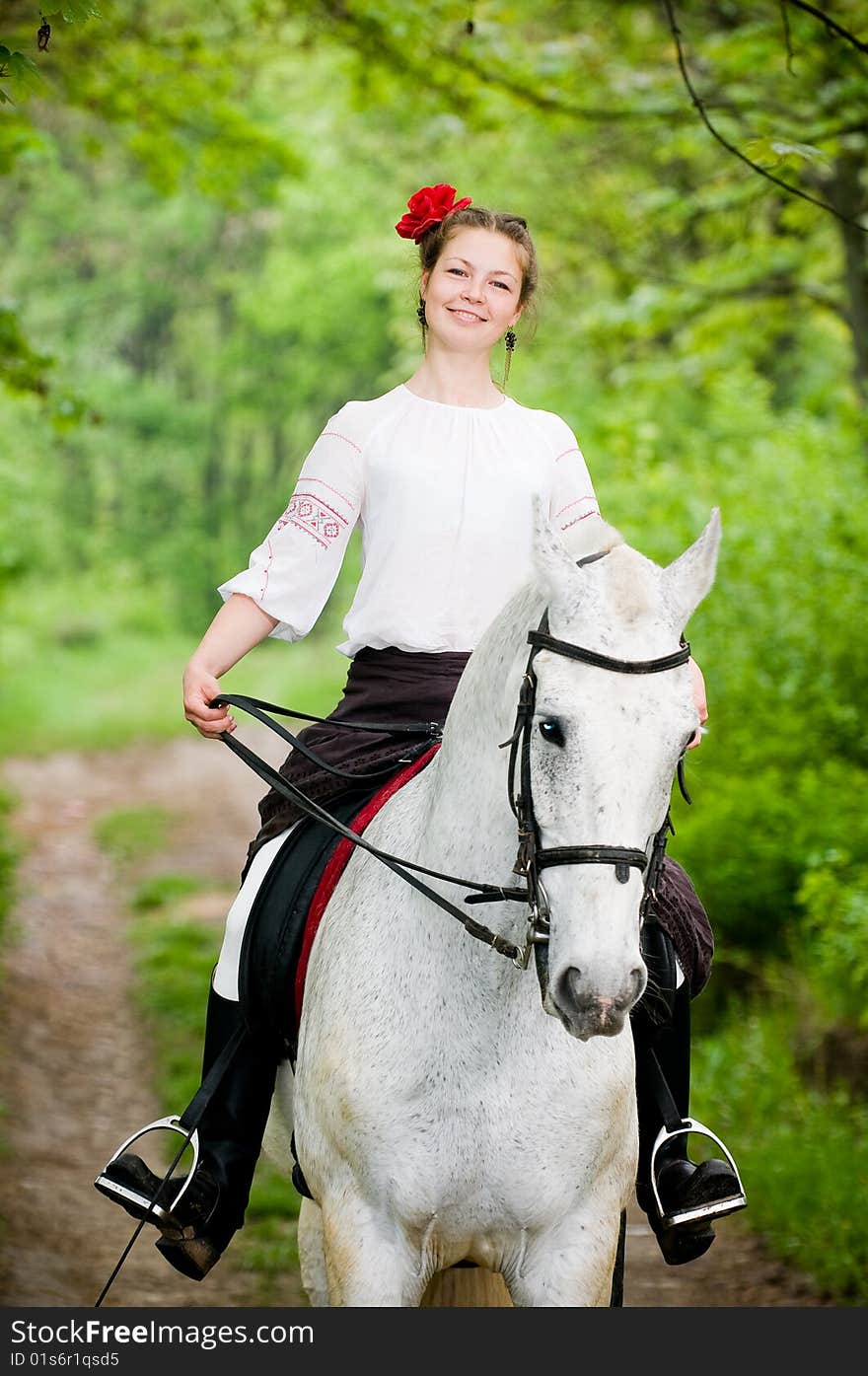 Smiling girl riding white horse in the forest