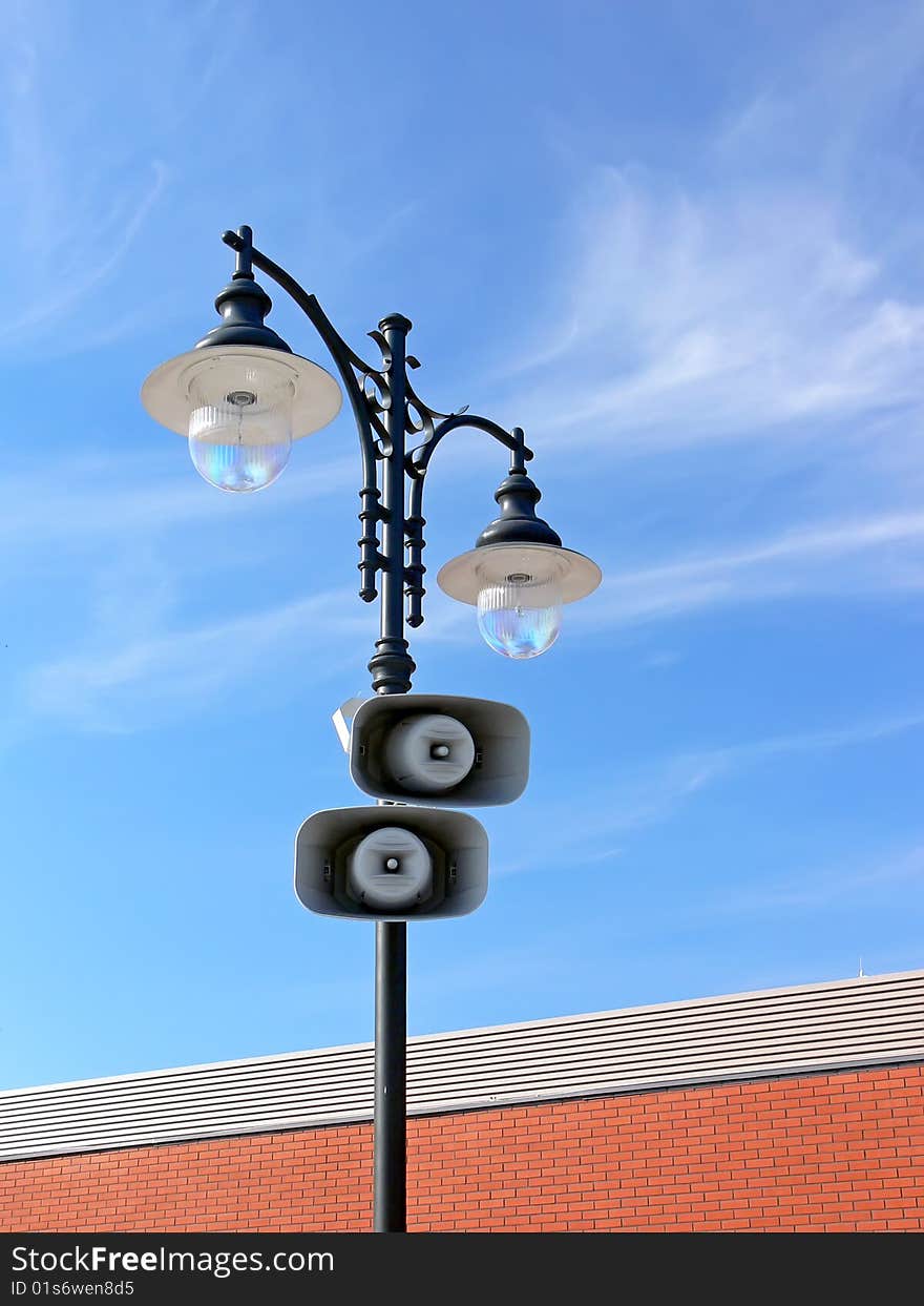 Two loud-speakers on retro lamppost with the red brick wall and blue sky in the background. Two loud-speakers on retro lamppost with the red brick wall and blue sky in the background.