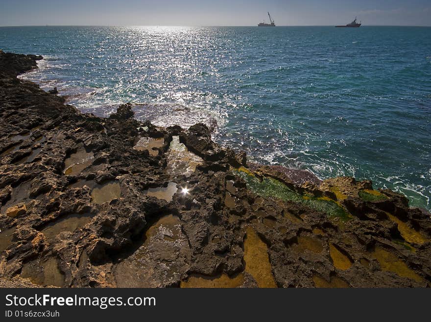 Seashore with colour rocks in foreground and nice blue water, ships on horizon