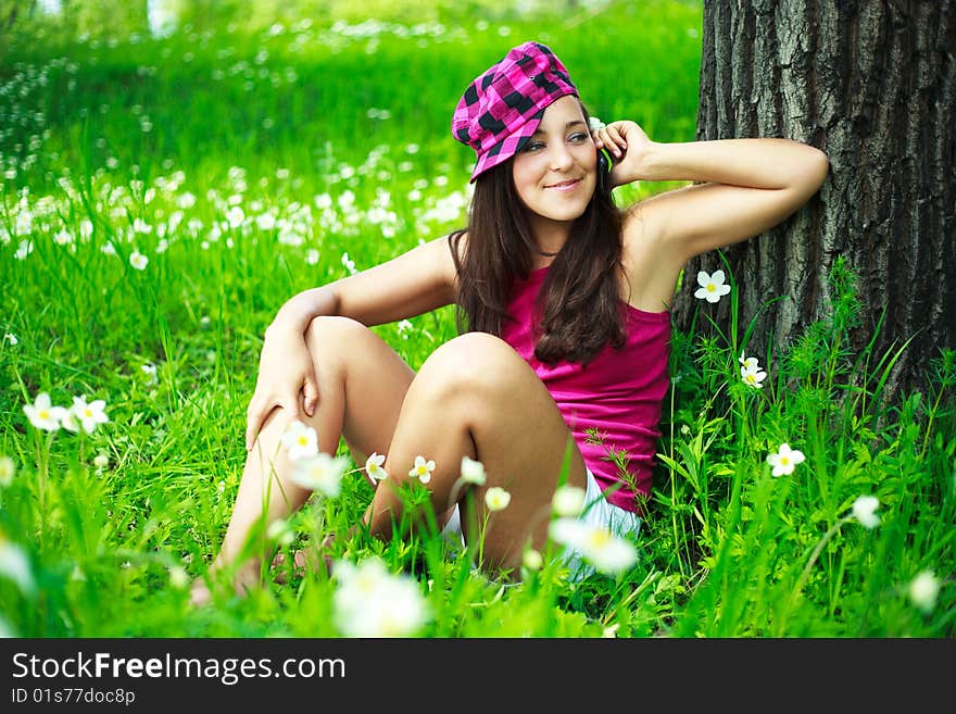 Beautiful brunette girl sitting on the grass in the park and talking on the cellphone. Beautiful brunette girl sitting on the grass in the park and talking on the cellphone