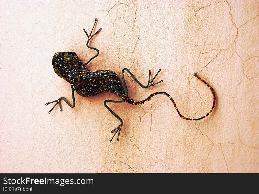 A beaded handmade lizard sitting on a wall in the sun. A beaded handmade lizard sitting on a wall in the sun