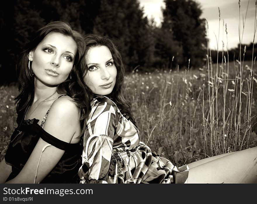 Two sensual girls sitting closely in the grass somewhere outdoors. Two sensual girls sitting closely in the grass somewhere outdoors