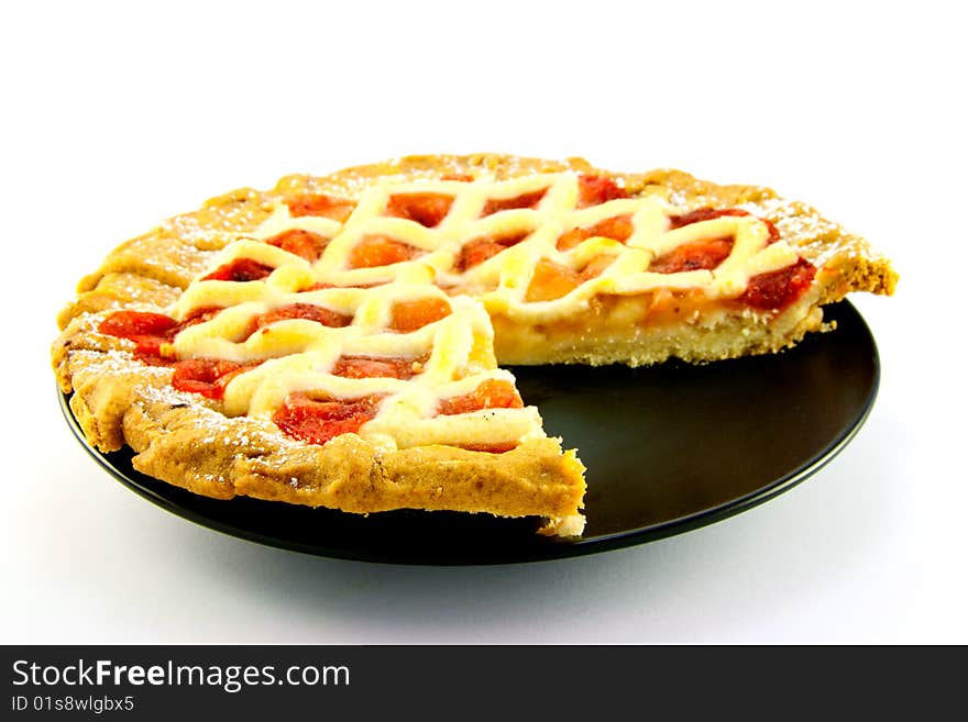 Whole apple and strawberry pie on a black plate with a slice missing on a white background. Whole apple and strawberry pie on a black plate with a slice missing on a white background