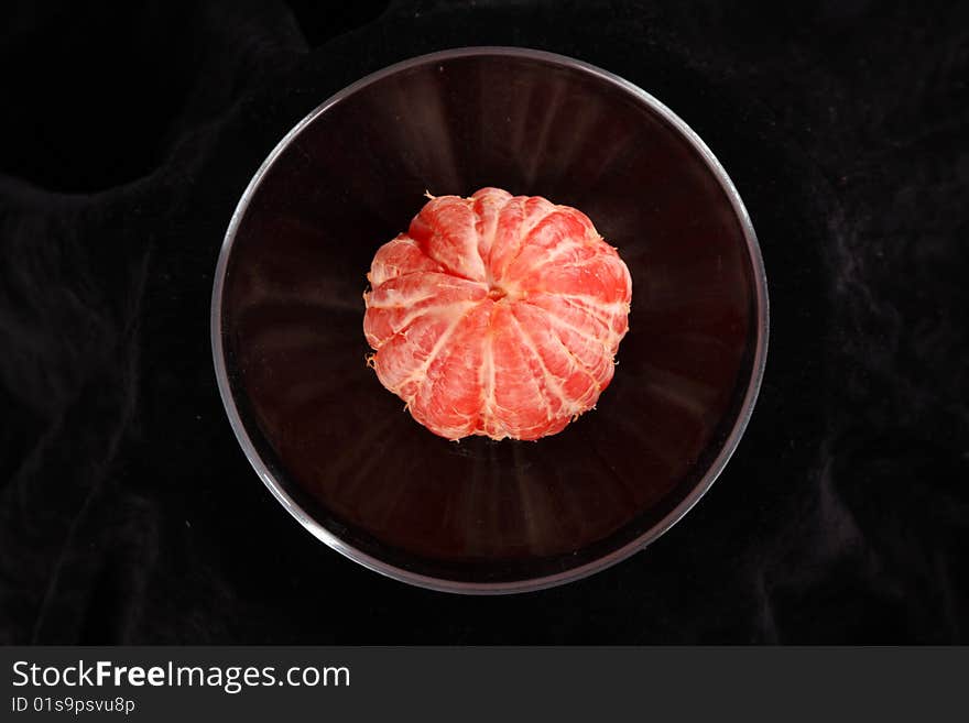 Grapefruit in the transparent plate against the black background, it is taken perpendicularly to the floor