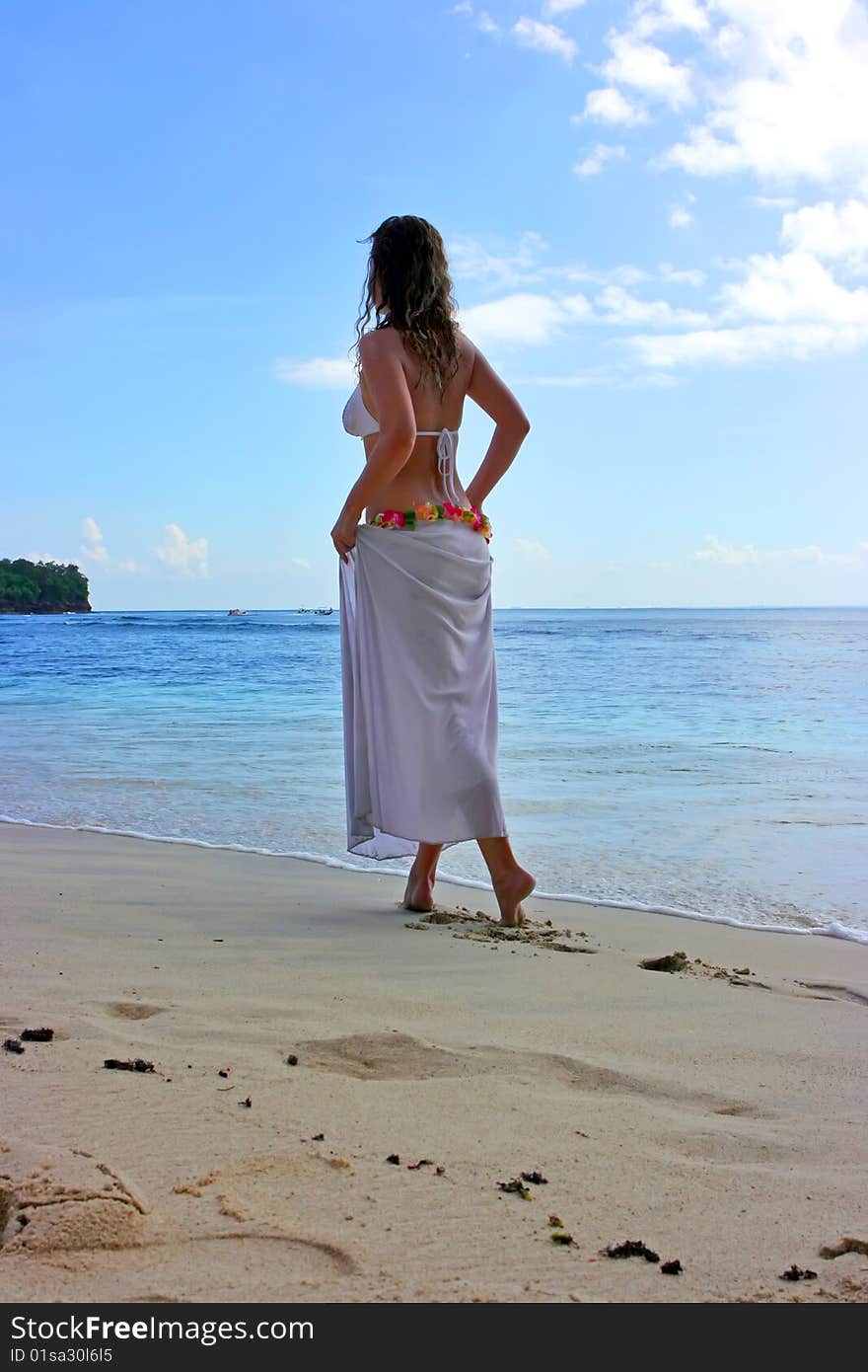 Beautiful brunette with long hair walking along the sand beach on Bali in Indonesia. Beautiful brunette with long hair walking along the sand beach on Bali in Indonesia