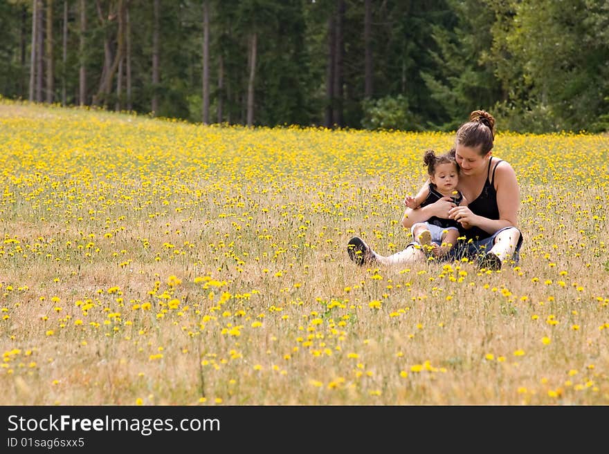 Young mother and her little girl sitting in a field of dandelions. Young mother and her little girl sitting in a field of dandelions