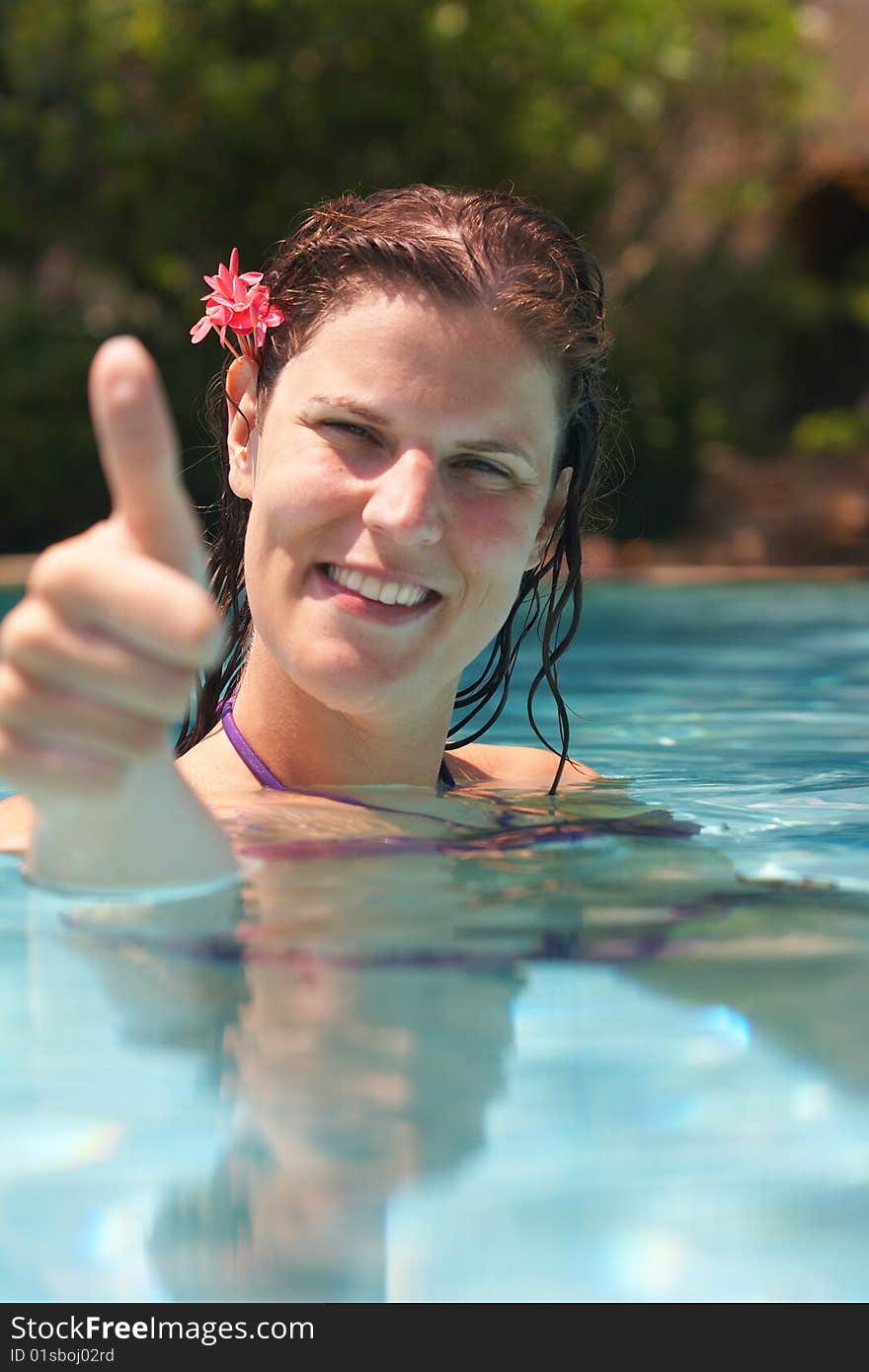 Young woman in a beautiful pool with palms in the background. She is showing a thumbs up sign. Young woman in a beautiful pool with palms in the background. She is showing a thumbs up sign.