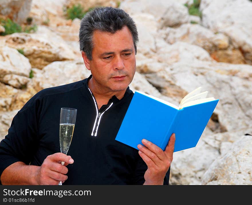 Man with a glass of champagne sitting outdoors reading a book. Man with a glass of champagne sitting outdoors reading a book