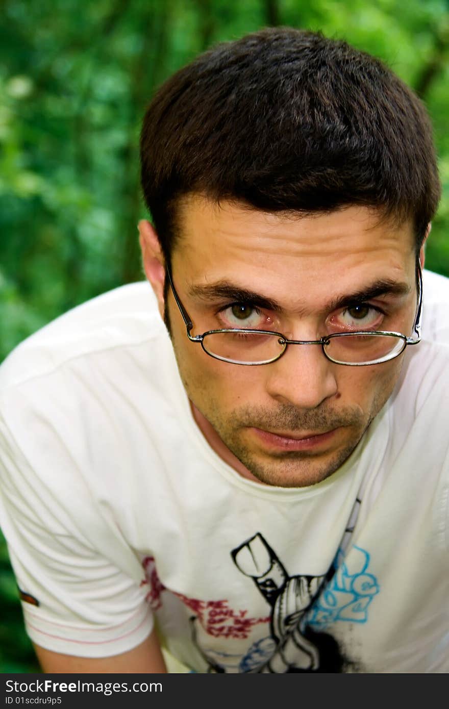 Portrait of young male in glasses and white t-shirt looking seriously, in the forest. Portrait of young male in glasses and white t-shirt looking seriously, in the forest