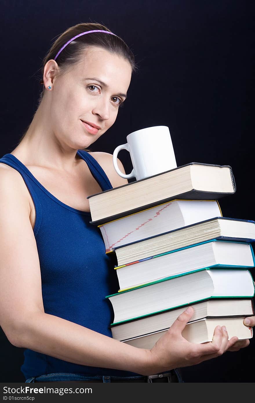 A young woman carrying a load of heavy books and coffee on a dark background. A young woman carrying a load of heavy books and coffee on a dark background.