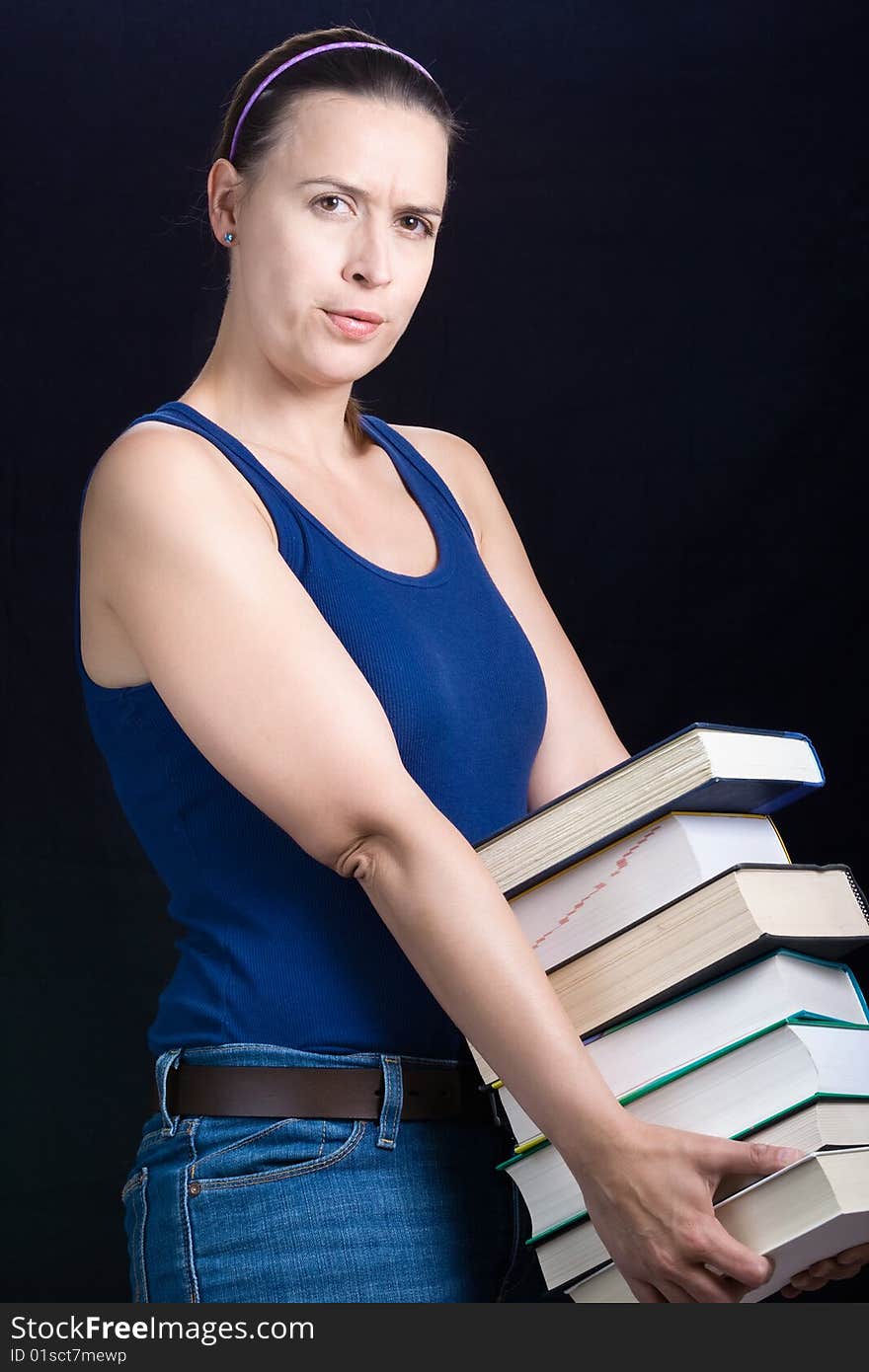 A young woman carrying a load of heavy books on a dark background. A young woman carrying a load of heavy books on a dark background.