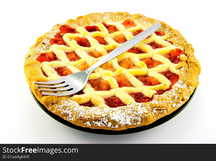 Whole apple and strawberry pie on a black plate with a fork on a white background. Whole apple and strawberry pie on a black plate with a fork on a white background