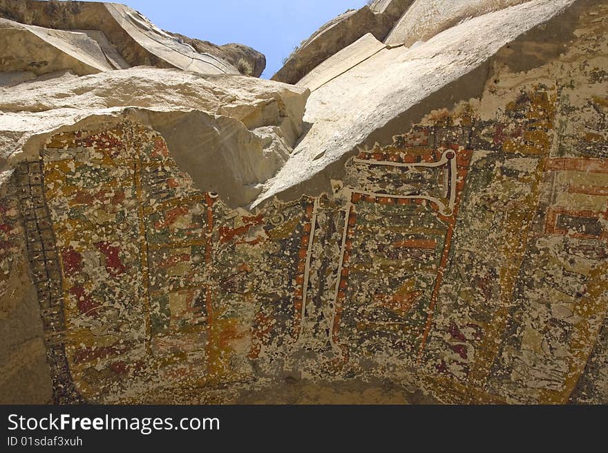 A chapel ceiling painted on the underside of rocks in Ilhara Canyon.  Early Christian painting of elaborate cross and biblical scenes.  Rock has eroded, leaving fractured artwork on the ceiling of the chapel.  View looking up of canyon rocks.  Blue sky. A chapel ceiling painted on the underside of rocks in Ilhara Canyon.  Early Christian painting of elaborate cross and biblical scenes.  Rock has eroded, leaving fractured artwork on the ceiling of the chapel.  View looking up of canyon rocks.  Blue sky.