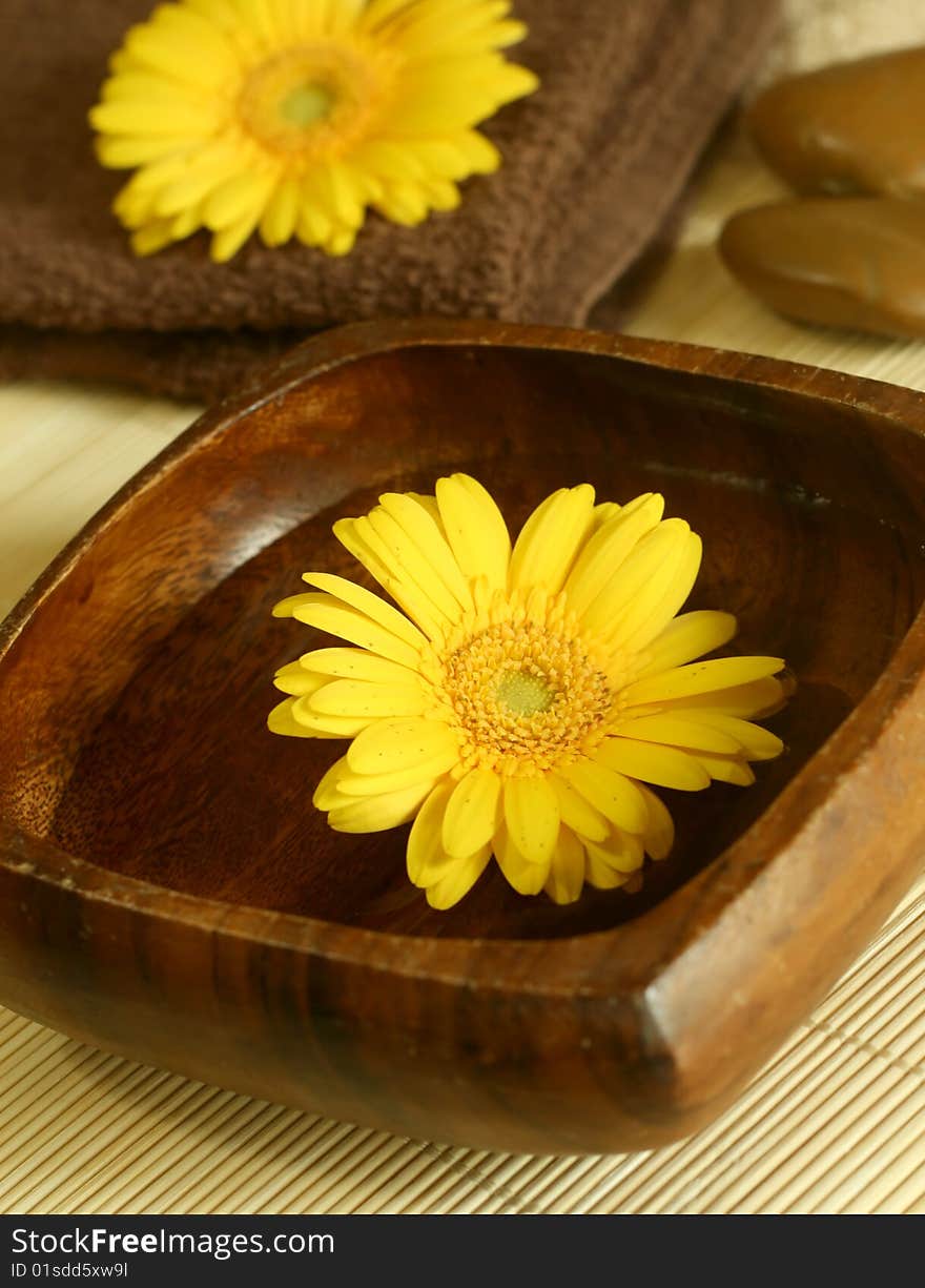 Yellow flower floating in wooden bow, towel and stones. spa background