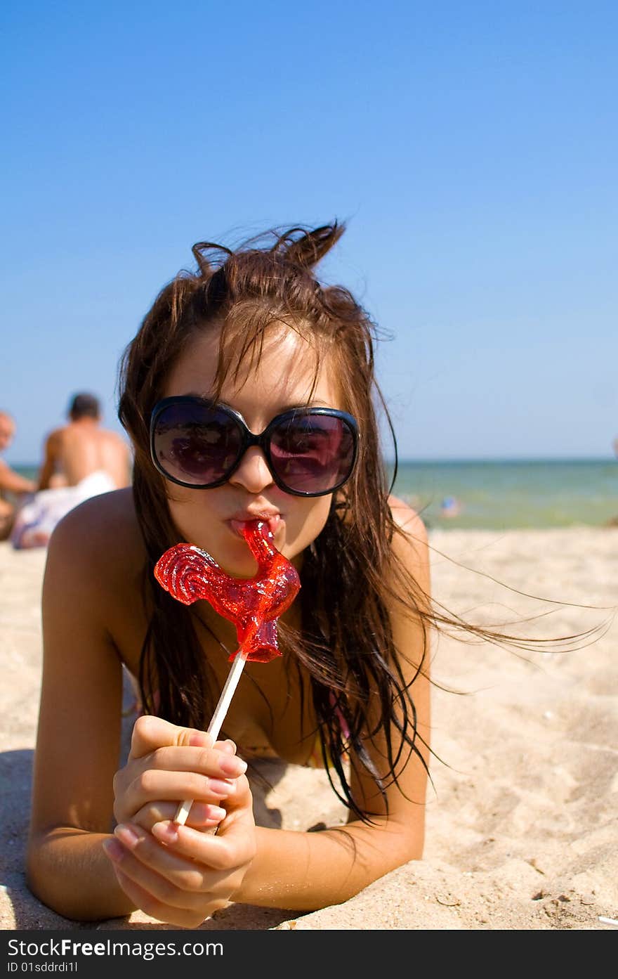 Girl in sunglasses with candy at the sea on the sand