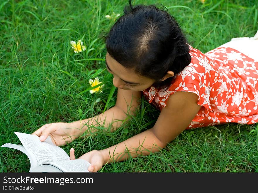 Lifestyle portrait of asian woman laying down on the green grass seems to enjoy her leisure time, reading her favorite novel. Lifestyle portrait of asian woman laying down on the green grass seems to enjoy her leisure time, reading her favorite novel