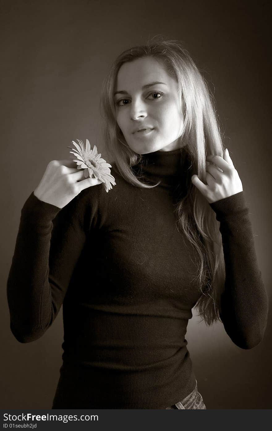 A young beautiful girl in dark jumper posing with a flower in her hand. A young beautiful girl in dark jumper posing with a flower in her hand