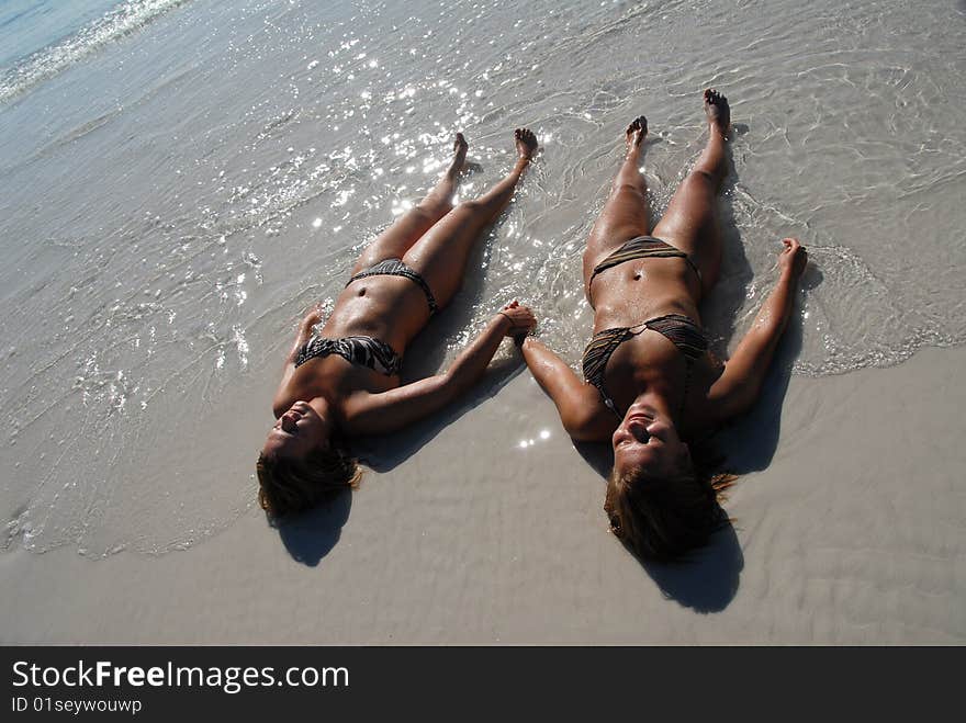 Two cute young girls lying on the beach holding hands