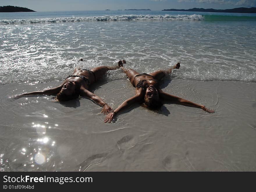 Two teenage girls lying in the water on beach doing snow angels. Two teenage girls lying in the water on beach doing snow angels