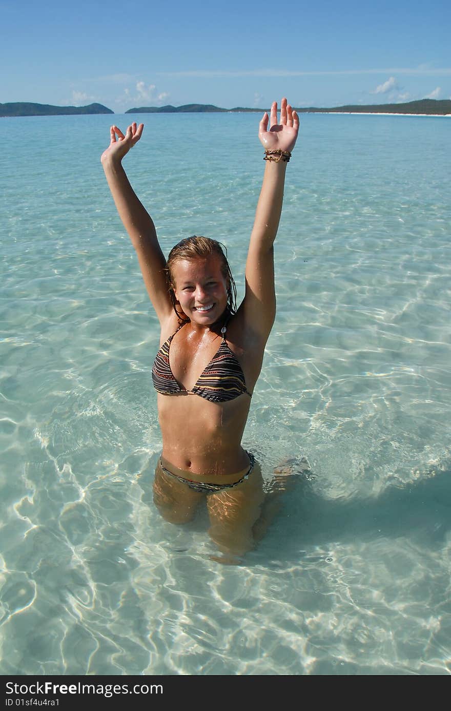 Beautiful young teenage girl standing in water at paradise beach with turquoise water raising hands above head