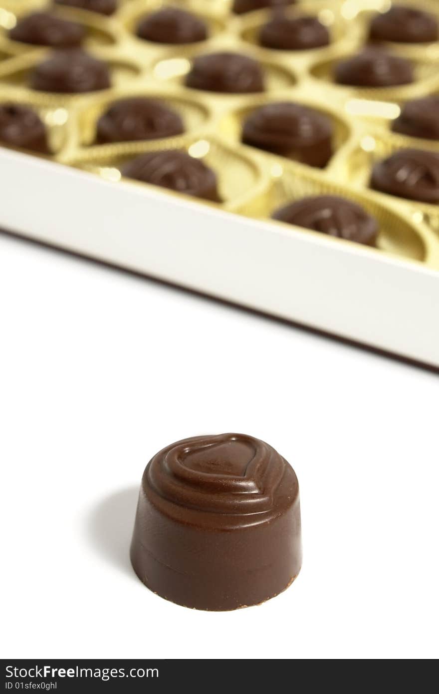 Chocolate sweet on a white background. Behind an open box of sweets