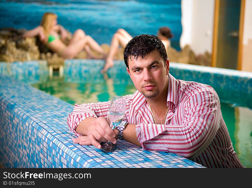 Portrait of a young man with a glass in the pool against the backdrop of two beautiful girls. Portrait of a young man with a glass in the pool against the backdrop of two beautiful girls