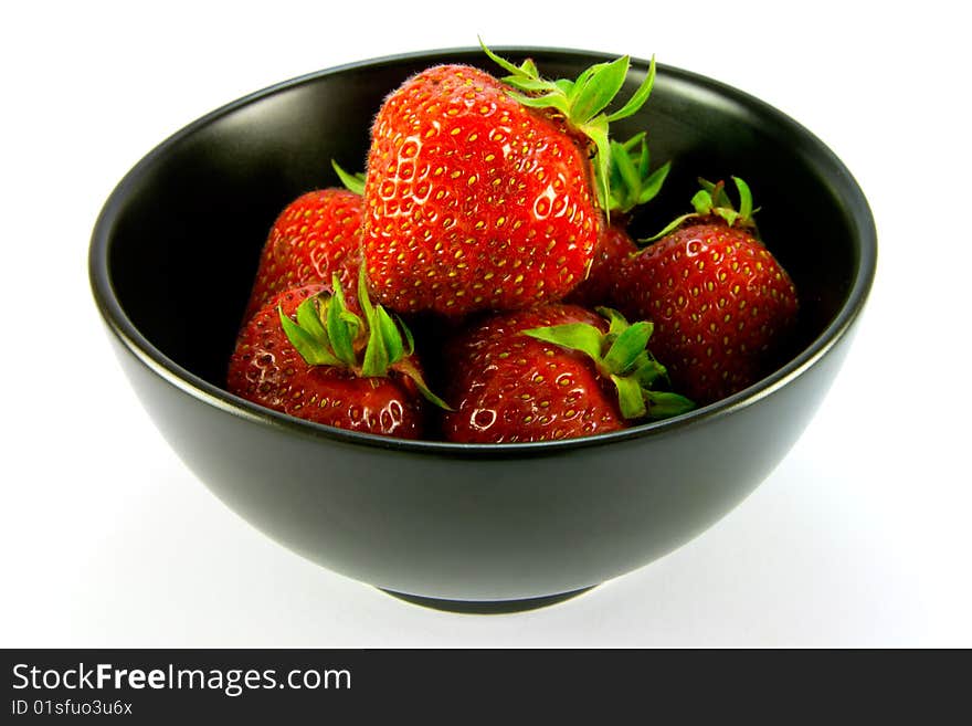 Whole red ripe strawberries in a black bowl on a white background